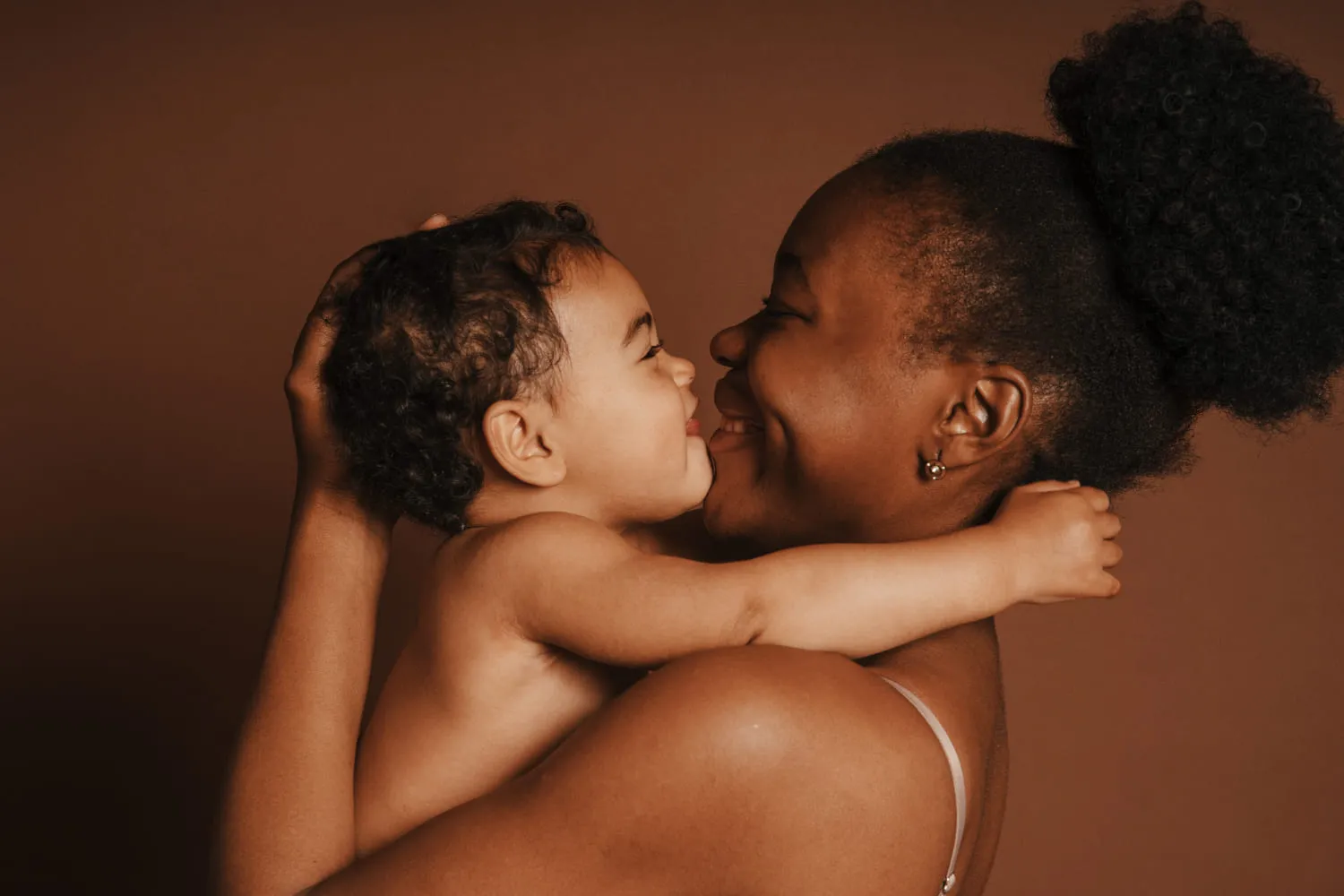 A mother smiling as she holds her baby up close against a warm brown backdrop