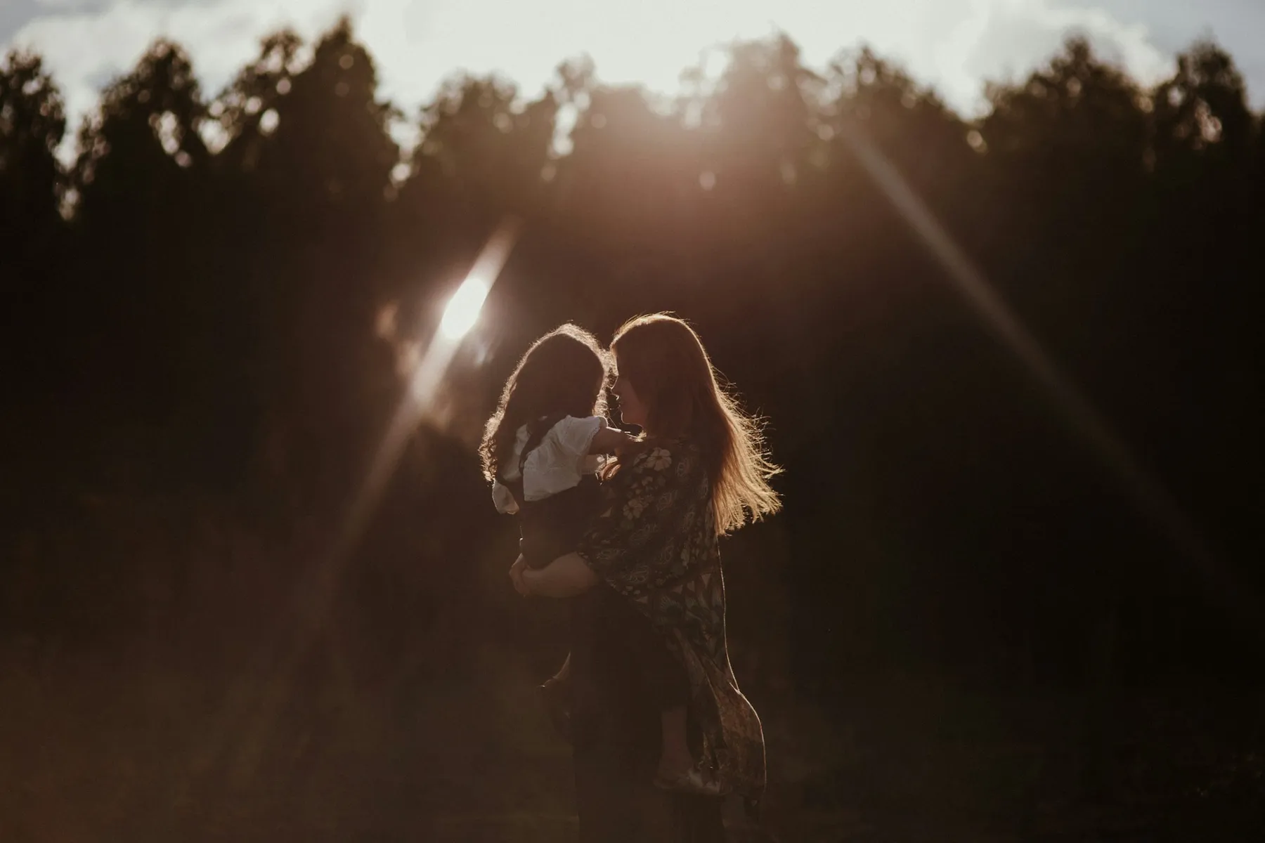 A mother lifting her child against a golden sunset sky