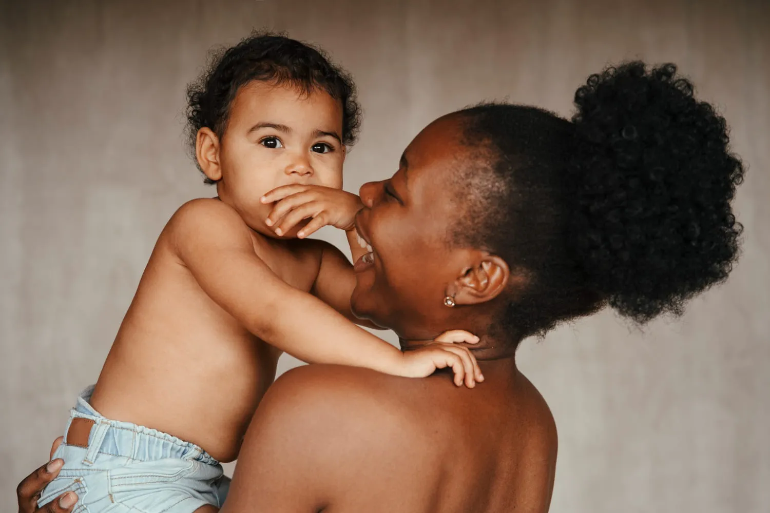 A mother holding her toddler close as the child reaches for her face