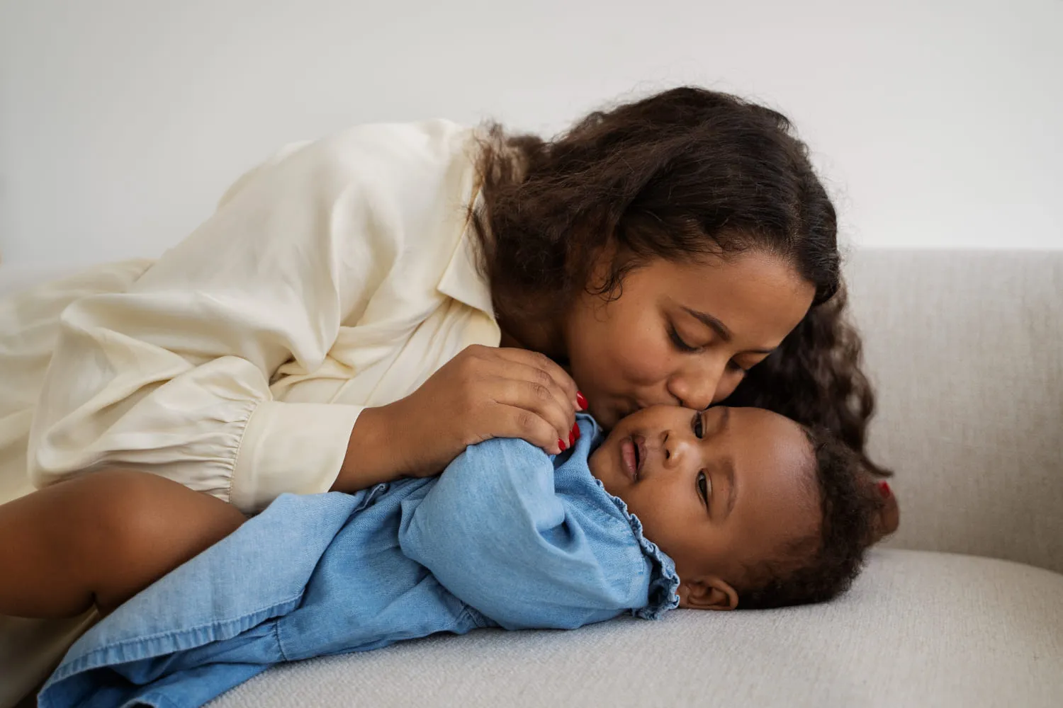 A mother leaning in to kiss her giggling child on a cream sofa