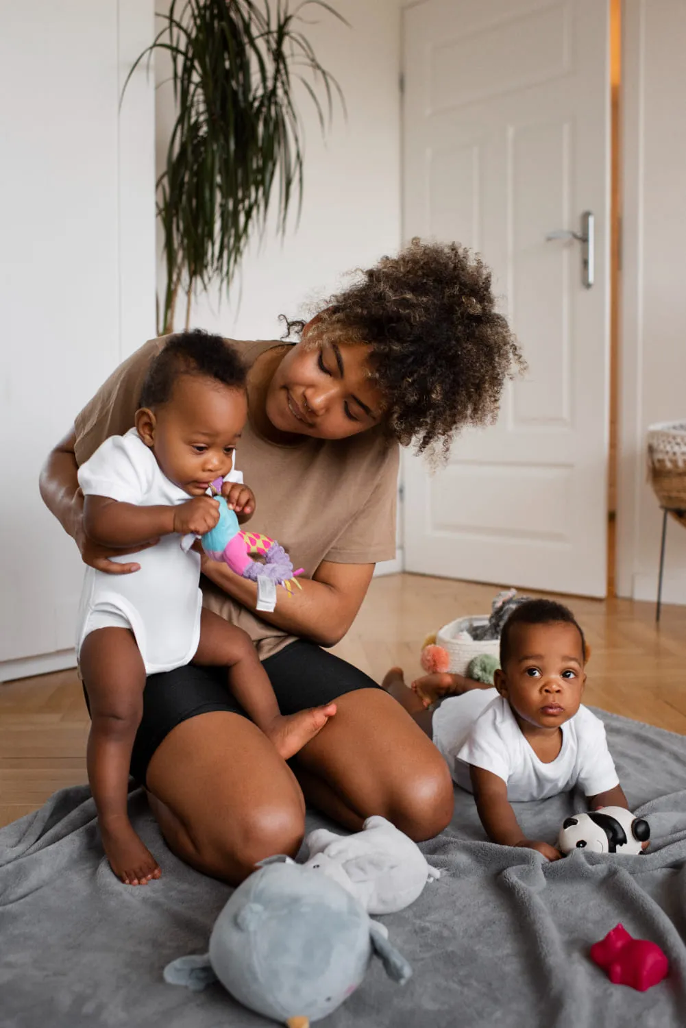 A mother sitting on a soft rug at home, playing with her two babies